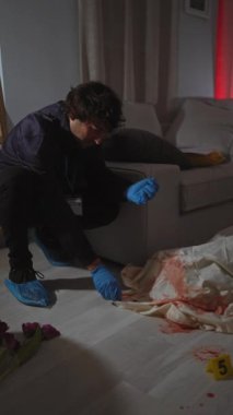 Adli tıp kıyafetli bir adam dramatik bir kapalı mekan suç mahallinde kan lekeleri ve numaralandırılmış işaretlerle kanıtları inceliyor..