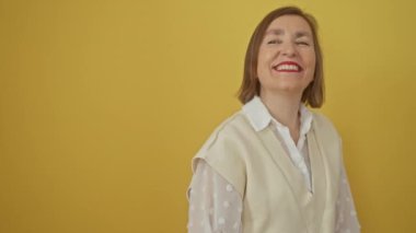 Kendinden emin orta yaşlı İspanyol kadın omzunun üzerinden bakarken doğal bir şekilde gülüyor, yüzünde izole edilmiş sarı bir arka plana karşı bir gülümseme var.
