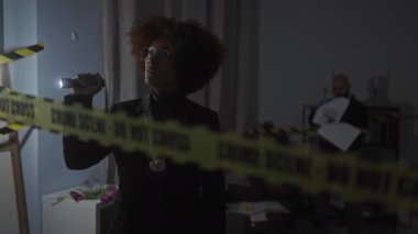 Elinde fener olan bir kadın dedektif kapalı alandaki loş bir suç mahallini araştırır ve bir adam kanıtları inceler..