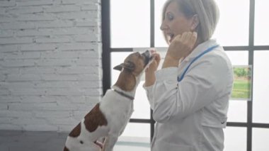 Veteriner kliniğinde küçük bir köpekle gülüp oynayan olgun sarışın bir kadın..