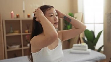 Genç bir kadın, arka planda mumlar ve bitkilerle kaplıcada saç ayarlıyor.