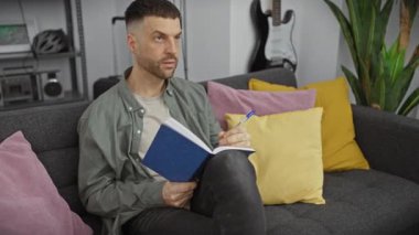 Yakışıklı, sakallı, İspanyol bir adam modern bir apartman dairesinde notlar alırken düşünüyor..