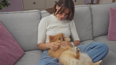 Kot pantolonlu bir kadın, rahat bir oturma odasında, koltukta pomeranian 'ına sarılıyor..