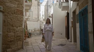 Genç bir İspanyol kadın gülüyor ve polignano 'nun büyüleyici taş caddelerinde yürüyor. Bir kısrak, puglia, İtalya, güneşli bir günde elinde örülmüş bir sepet tutuyor..