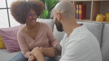 Gülümseyen ırklar arası bir çift, arka planda kitaplar olan bir kanepede rahat bir anın tadını çıkarır..