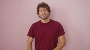 Gergin ve şüpheci İspanyol tişörtü giyen genç adam kollarını çapraz yapıp yüzünde negatif bir ifade bırakıyor. Pembe arkaplanda izole bir şekilde duruyor