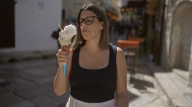 Genç İspanyol kadın, Puglia, İtalya 'nın eski güzel sokaklarında güneşli bir günde büyük bir külahta dondurma ve krema yiyor..