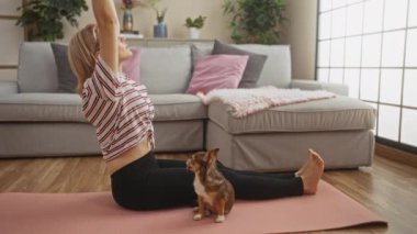 Sarışın genç bir kadın oturma odasında yoga minderinin üzerine uzanır. Yanında Chihuahua 'sı ile birlikte. Kapalı mekan ışıklarının altında..