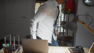 Dizüstü bilgisayarı, dosyaları, kravatı, gözlükleri, rafları, sandalyesi, saati ve lambası olan Asyalı genç bir adam profesyonel bir ayar çiziyor..