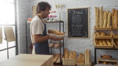 Önlük giymiş genç bir adam, arka planda bir fiyat tahtası ve raflı sıcak bir fırında bir sepet ekmek tutuyor.