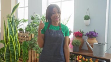 Neşeli Afro-Amerikan kadın çiçekçi, önlüklü, çiçekçide dikiliyor, 