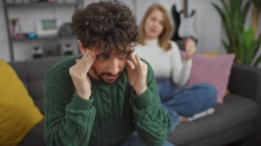Baş ağrısı olan sıkıntılı bir adam ve modern bir oturma odasında birlikte oturan endişeli bir kadın..