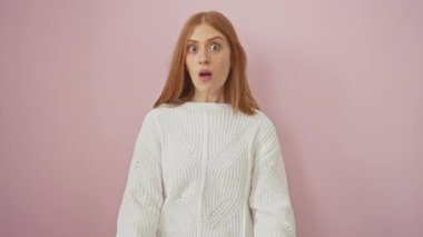 Şok olmuş, süveterli genç bir kadın, elleri hatanın üzerindeyken ağzını kapatıyor, pembe arka planda izole edilmiş bir sırrı içine çekiyor.