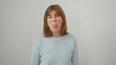 Süveter giyen küstah orta yaşlı kadın eğlenceli bir jest yapmak için dilini dışarı çıkarıyor. Mutlu, eğlenceli ifade beyaz arka planda izole edilmiş neşeli ruhunu sergiliyor.