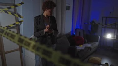 Dedektif kadın kapalı mekan suç mahallini araştırıyor. Evin içinde notlar alıyor. Çerçeveye bantla yapıştırıyor..