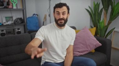 Neşeli orta yaşlı adam mutlu mesut dört parmağını evde gösteriyor, beyaz tişört giyerken kendine güvenen bir gülümseme gösteriyor.