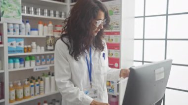 Profesyonel bir kadın eczacı, iyi aydınlatılmış eczane içlerindeki ilaç rafları arasında dokümanları inceliyor.