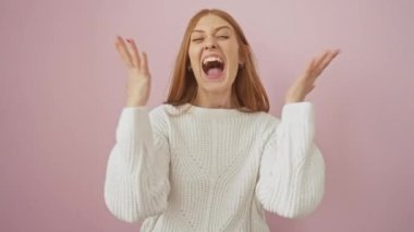 Süveter giyen neşeli kızıl saçlı kız, elleri havada, kazanmaktan mest olmuş! Evet, genç bir bayan kazanan, pembe arka planda gülücüklerle kutluyor..