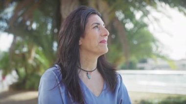 Güneşli bir parkta palmiye ağaçlarıyla tefekkür eden olgun İspanyol kadın.