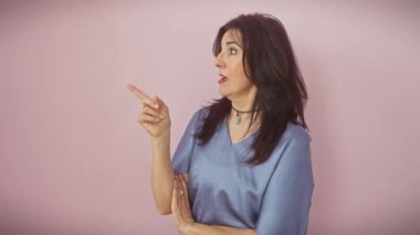 Neşeli orta yaşlı İspanyol kadın pembe arka planda tek başına duruyor, neşeli bir el hareketi ile neşeyle yüzünü aydınlatan yürek ısıtan bir gülümseme ile kenarı gösteriyor..