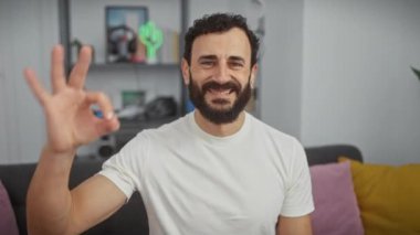 Cheerful middle age man, looking confident at home, wearing a white t shirt, flashing a successful 'ok' sign with hand and fingers. a positive expression of pure success!