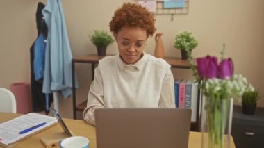 Neşeli Afro-Amerikalı kadın evde, neşeli bir şekilde işaret veriyor, masada otururken gülümsüyor..