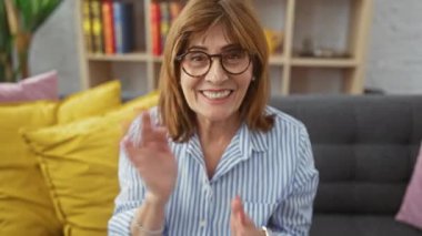 Gözlüklü, çizgili tişörtlü, evdeki kanepede oturan gülümseyen son sınıf öğrencisi.