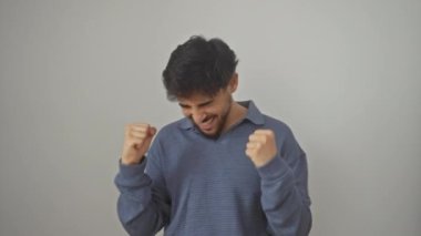 Heyecanlı genç Arap adam başarıyı kutluyor, ayakta duruyor, sevinç çığlıkları atıyor ve izole beyaz arka planda bir jest kazanıyor.