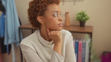 Afro-Amerikan kadının doğal bir duruşu var. Ev masasında oturuyor ve gülümsüyor.