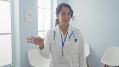 Kendine güveni tam orta yaşlı bir kadın doktor. Parlak bir klinikte el kol hareketi yapıyor.