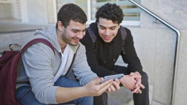 Şehir caddesinde birlikte akıllı telefona bakan iki adam güler..