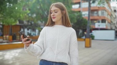 Şehirde akıllı telefon kullanan gülümseyen kadın sıradan kıyafetler giyiyor..