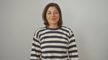 Güzel orta yaşlı İspanyol kadın mutlu bir şekilde gülümsüyor, çizgili bir kazak giyiyor, kollarını kavuşturuyor, beyaz izole edilmiş arka planda kendinden emin görünüyor. Başarılı bir yaşam tarzının pozitif, doğal ifadesi