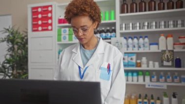 Üniformalı Afro-Amerikan kadın eczacı. Eczanede mükemmel dişleriyle gülümsüyor.
