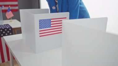 Kendine güvenen bir kadın, Amerikan oy kullanma merkezinde bayrak ve kulübelerle oy veriyor..