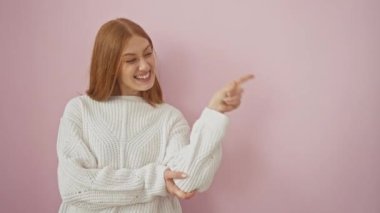 Yüzünde kocaman bir gülümsemeyle ayakta dikilen, elleri ve parmaklarıyla kameraya bakan genç, kızıl saçlı kadın. izole edilmiş pembe arkaplan