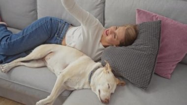 Gündelik kıyafetli genç bir kadın, köpeğiyle rahat bir oturma odasındaki kanepede vakit geçirmekten zevk alıyor. Selfie çekiyor.