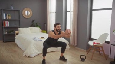 Sakallı adam yatak odasında kettlebell ile egzersiz yapıyor, evde kararlılık ve zindelik gösteriyor..