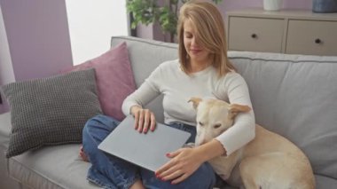 Genç bir kadın evinde dizüstü bilgisayarıyla çalışıyor. Köpeği yanında, kanepede. Kapalı bir ev sahnesini resmediyor..