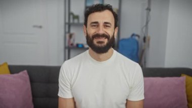 Kendine güvenen olgun bir adam, beyaz tişörtle pozitiflik yayıyor. Sersemletici mutlu yüzü serin bir gülümseme sergiliyor, evdeki neşeli atmosferi arttırıyor..