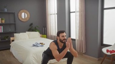 Orta yaşlı, sakallı bir adam modern bir yatak odasında dambılı ve şık bir dekorasyonla egzersiz yapıyor..