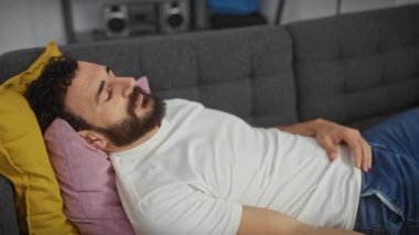 Evde üzgün orta yaşlı bir adam, beyaz tişört giyiyor, gözleri kollarıyla çaresizlik içinde. Saklanma, görme engelleme, ciddi bir ifade.