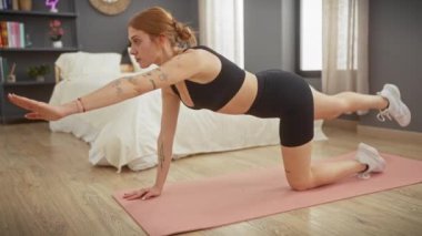 Odaklanmış genç bir kadın modern bir yatak odası ortamında pembe bir paspasla yoga yapıyor..