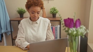 Afrika kökenli Amerikalı bir kadın evde çalışırken yorgun hissediyor. Çiçekli ve bitkilerle dolu bir odada dizüstü bilgisayarla oturuyor..