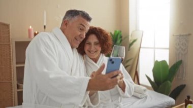 Orta yaşlı bir çift evde bornozla spa gününün tadını çıkarıyor. Elinde bir bardak şarapla görüntülü sohbet ederken gülümsüyorlar.