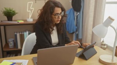 Olgun bir kadın, dijital tablete odaklanmış, üretkenliği ve profesyonelliği somutlaştıran bir ev ofisinde dizüstü bilgisayarla çalışır..