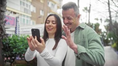 Mutlu bir çift şehrin bir caddesinde birlikte selfie çekiyor, açık hava ortamında ilişkilerini sergiliyorlar..