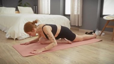 Dövmeli genç bir kadın yatak odasında yoga yapıyor. Huzurlu bir evde esneklik ve sükunet gösteriyor..