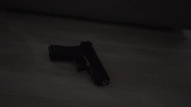 Ahşap bir yüzeyde bir erkeğin tabancaya uzandığı karanlık bir sahne belirsizlik ve tehlikeyi akla getiriyor..