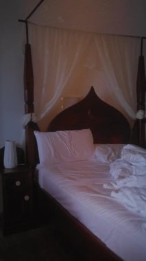 Loş bir odada dağınık beyaz çarşaflarla zarif bir şekilde örtülmüş dört posterli yatak.